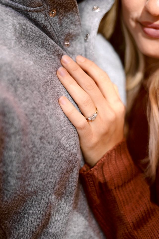 Close-up of an engagement ring on a hand wearing a brown knit sweater.