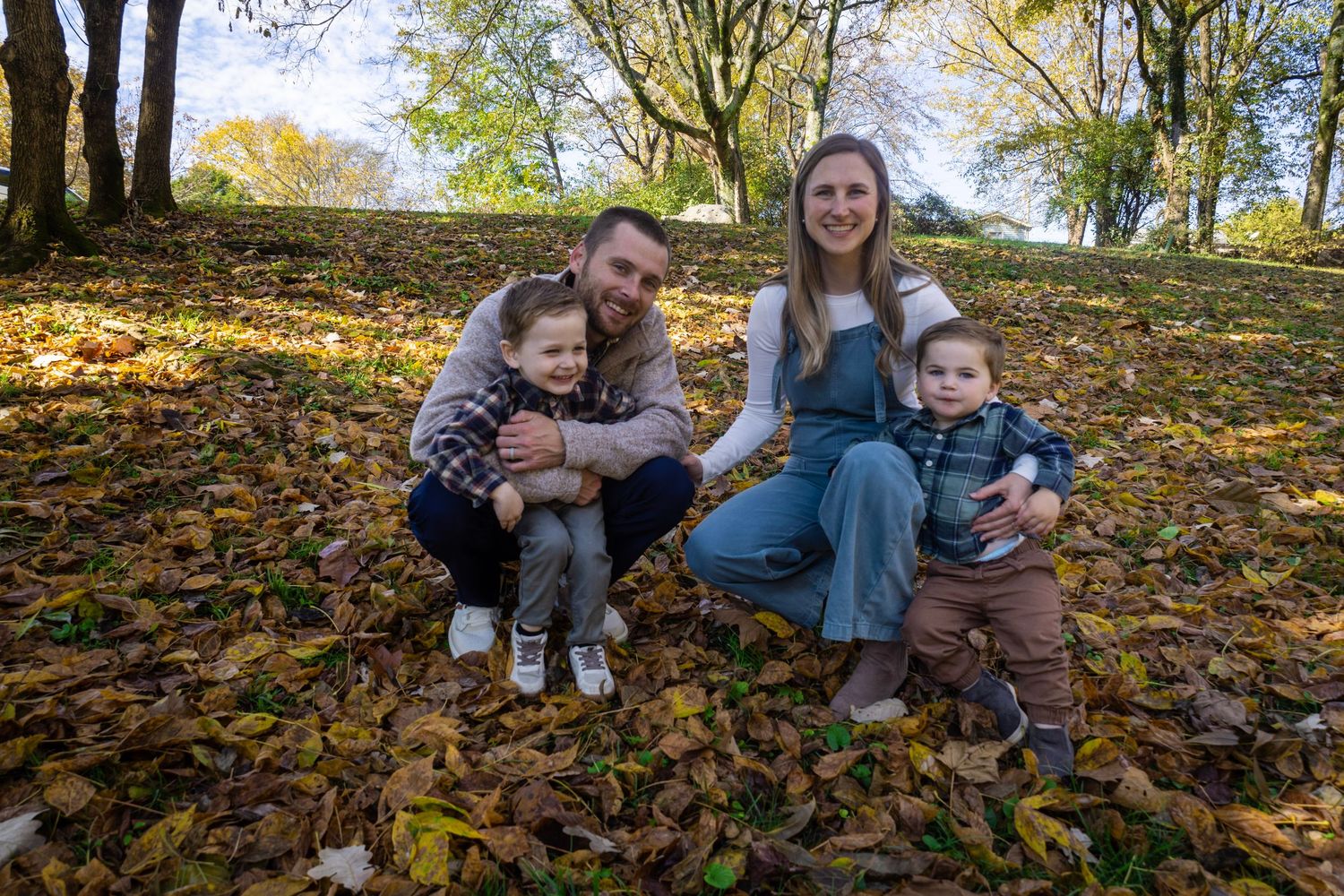 A family sits together on fallen autumn leaves in a park setting.