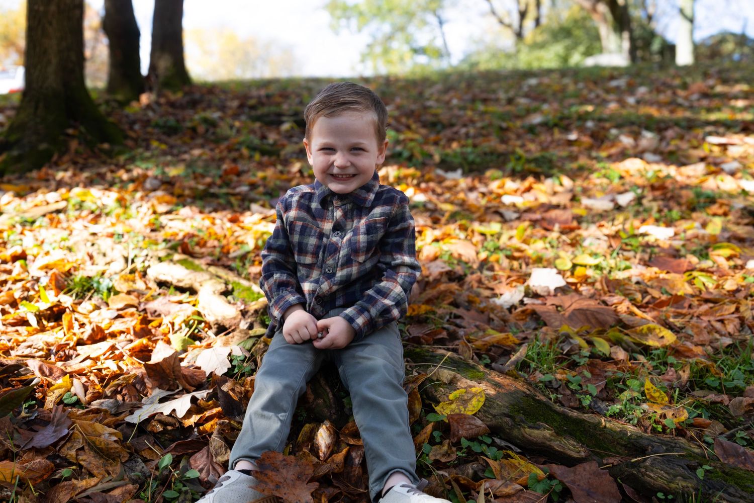 Child playing in fallen autumn leaves near water.