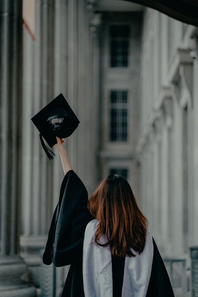 Graduates raising their caps in celebration against a classical building backdrop.