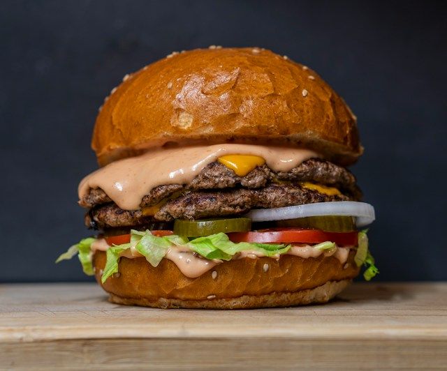 Professional food and product photography featuring a double cheeseburger with fresh toppings against a dark background.