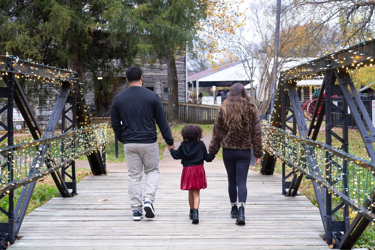 A family walks hand in hand across a decorated bridge with twinkling lights.