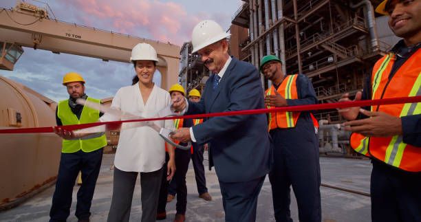 Grand opening photography of an executive cutting a red ribbon at an industrial facility, surrounded by employees in safety gear.
