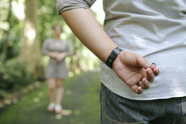 A person's hand with a smart watch holds something behind their back in an outdoor setting.