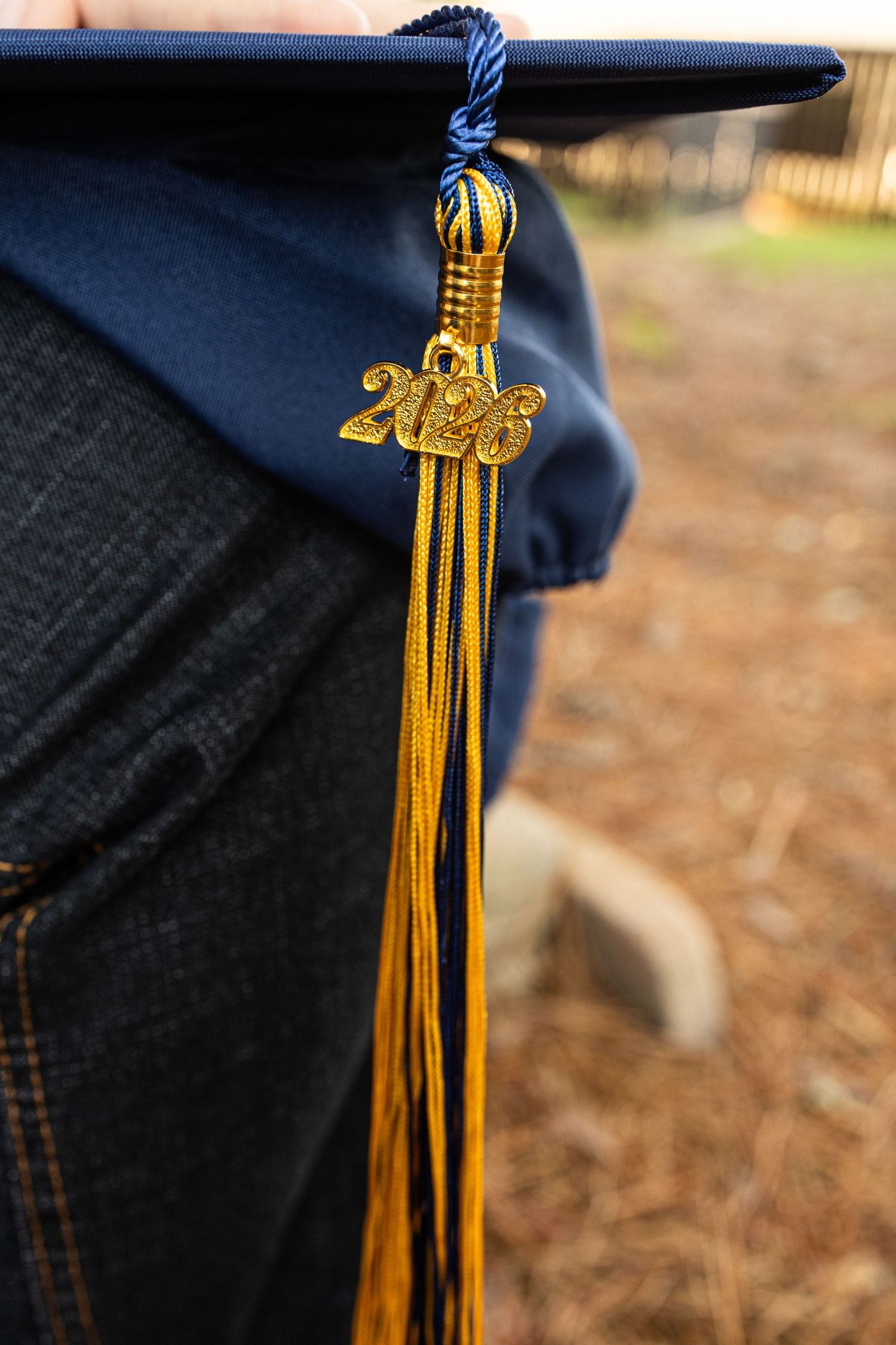 Close-up of a navy blue 2023 graduation cap with gold tassel held by a graduate in jeans outdoors.