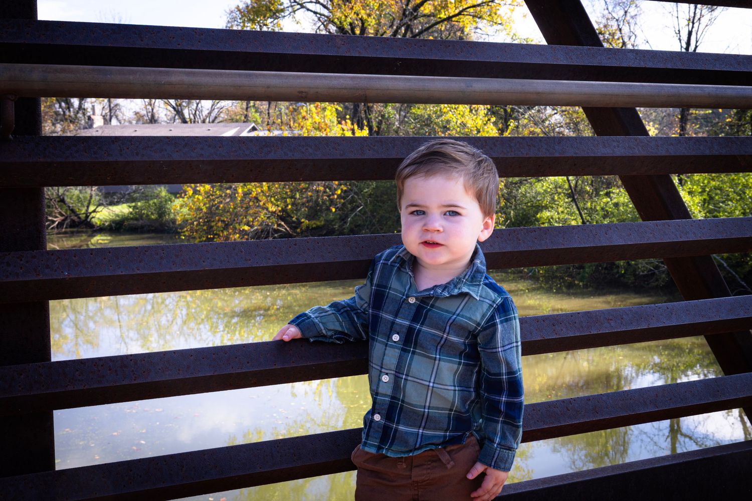 Young child sitting on wooden bridge railing overlooking water.