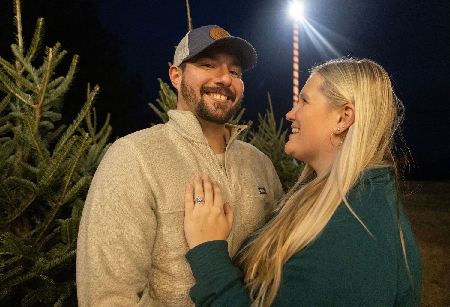 Romantic evening photoshoot with couple laughing under string lights near pine trees.