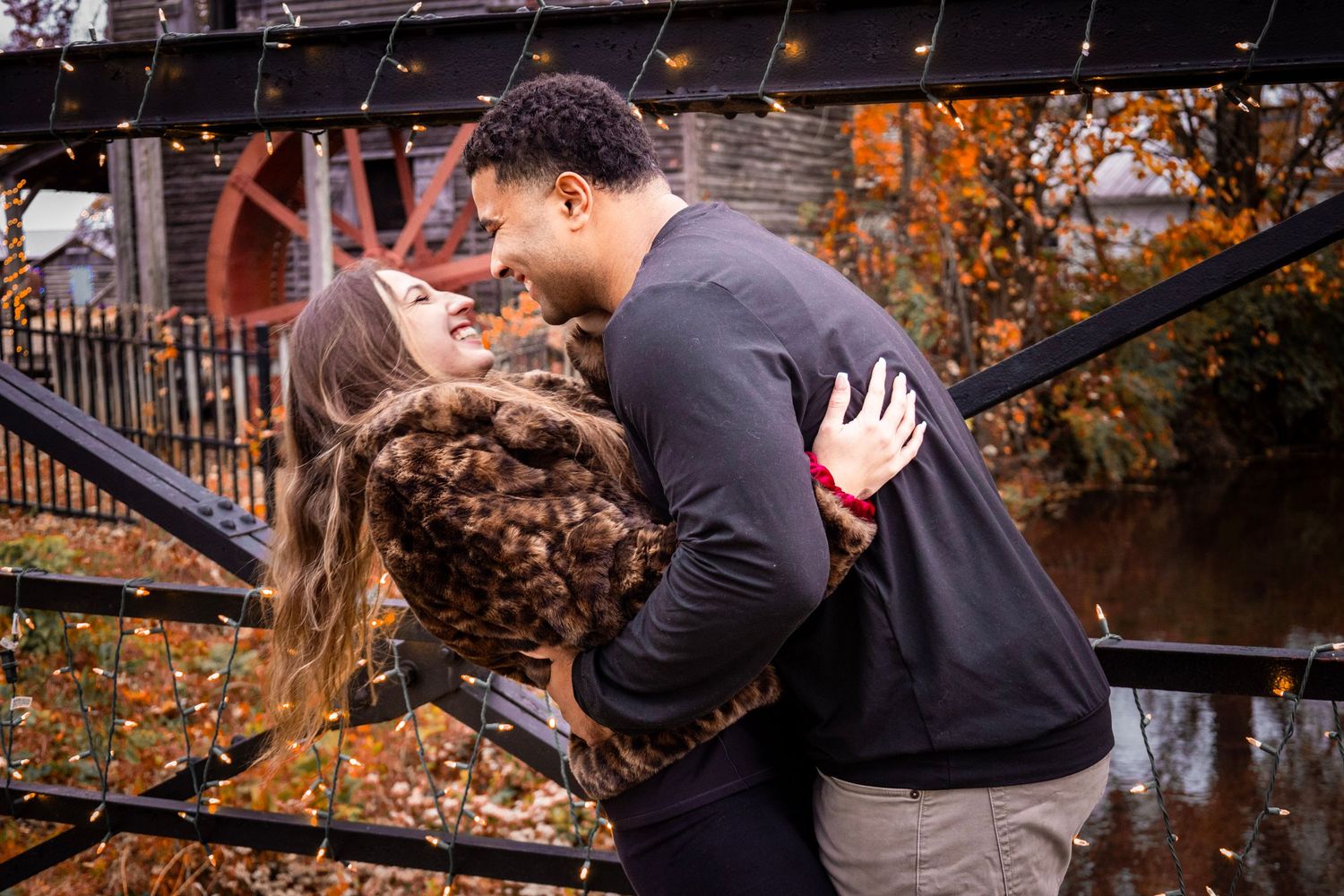Couple sharing intimate moments during fall engagement photoshoot with string lights.