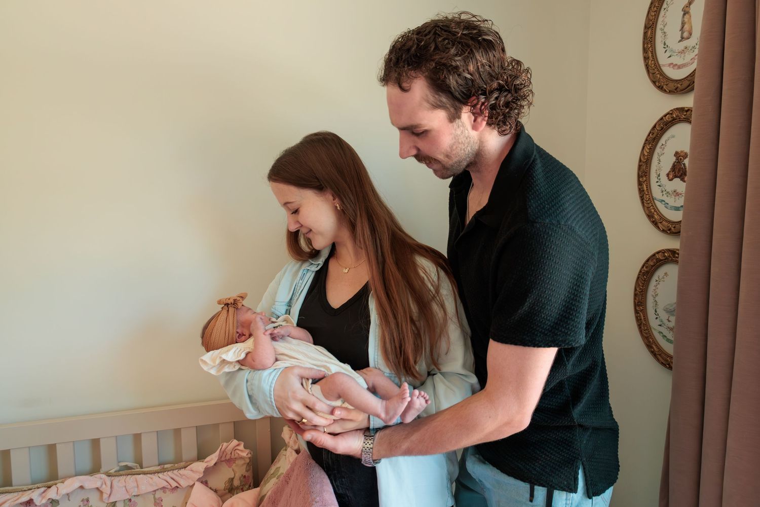 New parents admiring their newborn baby in a nursery, with the mother cradling the infant in a pink blanket.