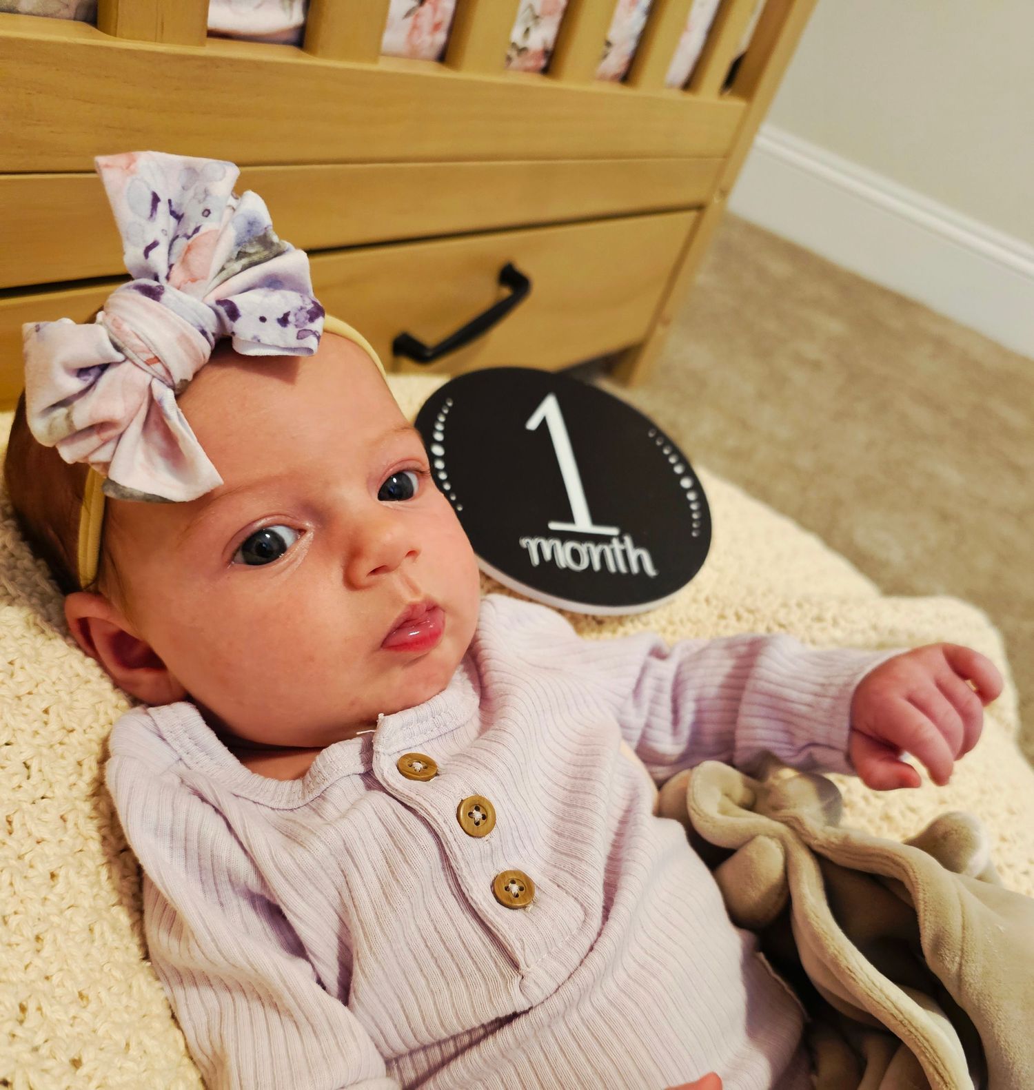 Baby wearing pink sweater and bow lying on blanket with milestone markers.