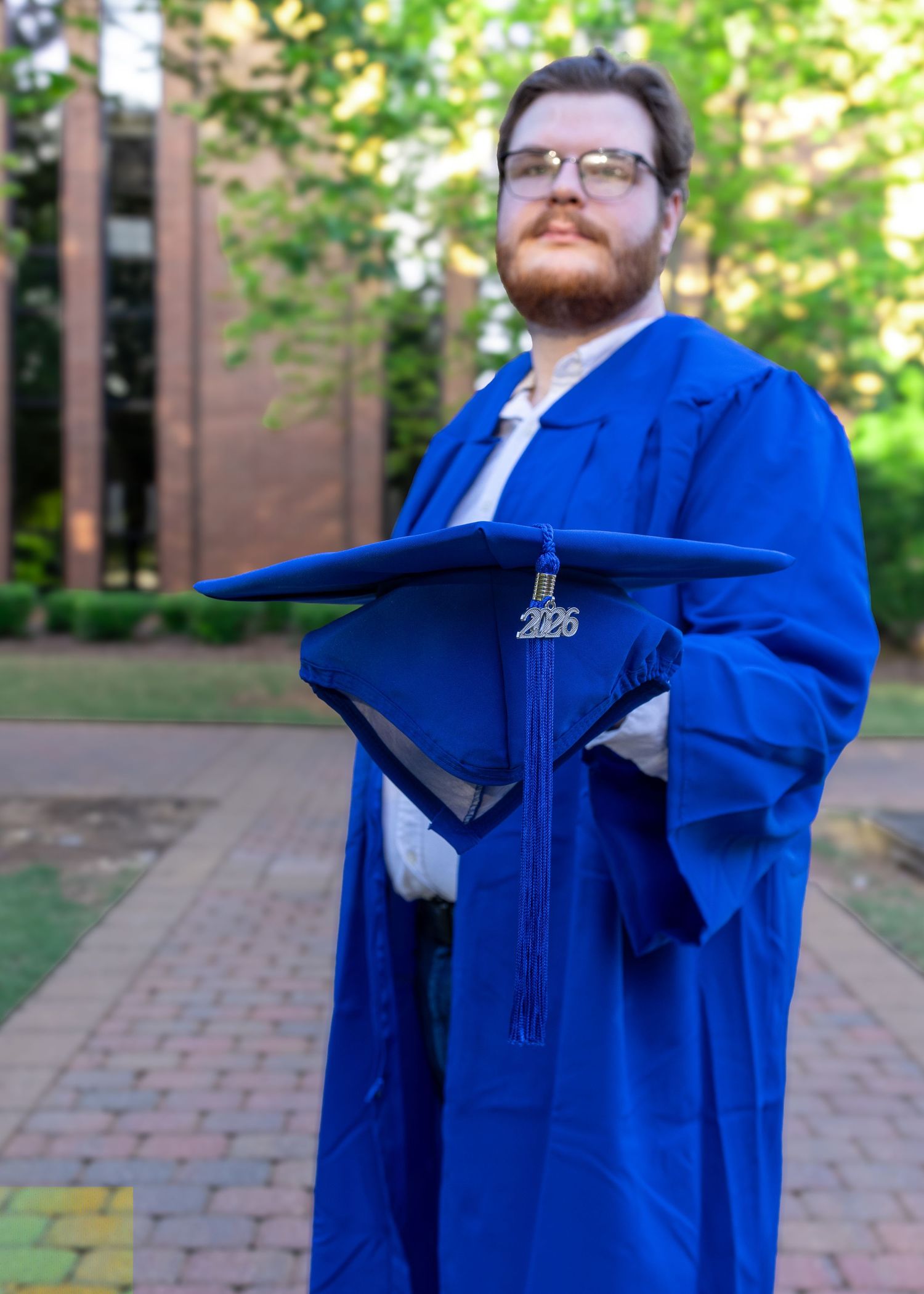 High school senior in a blue graduation cap and gown during a senior photography session near Madison, Alabama.