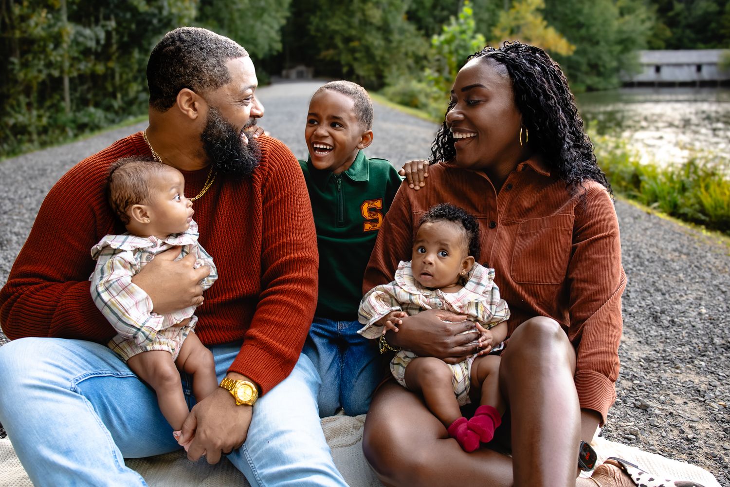 Happy Black family with two babies and a child sitting outdoors, smiling and bonding together in nature.
