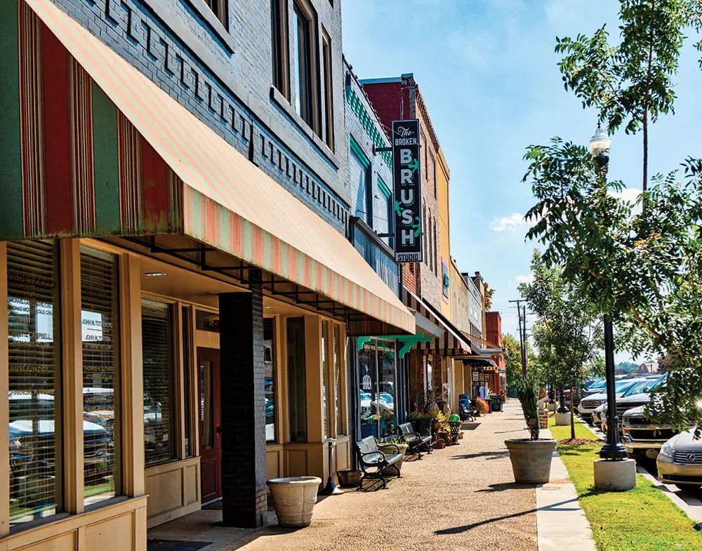 Charming small-town main street with colorful awnings, brick storefronts, and a Brush sign on a sunny day.