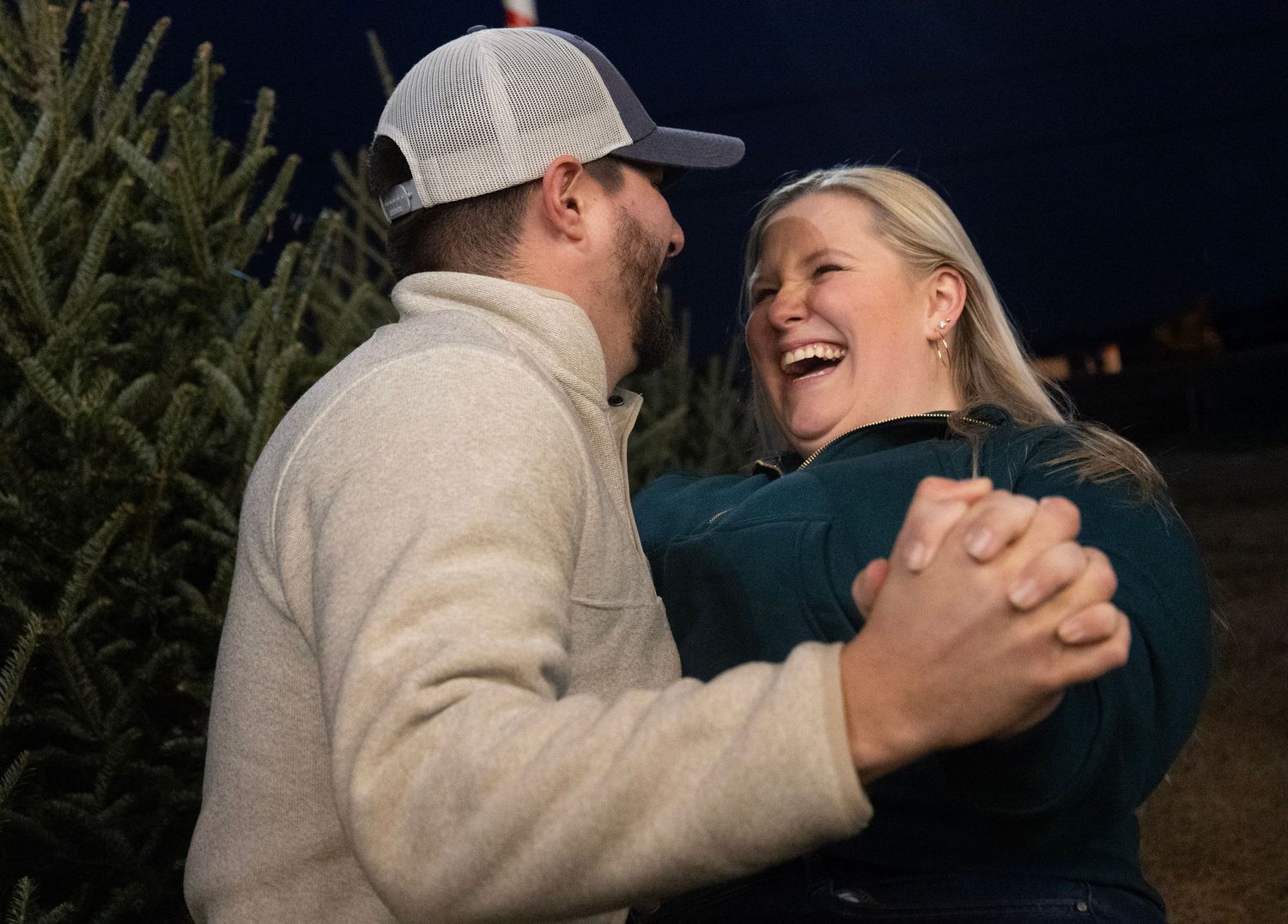 A romantic couple dances together at night with evergreen trees visible in the background.