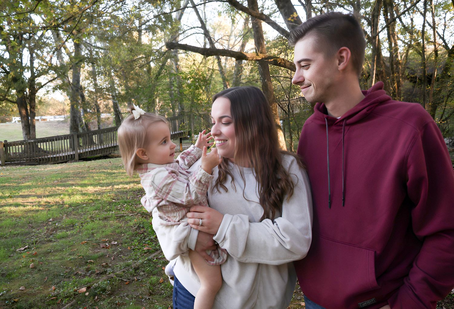 Young family with baby girl enjoying outdoor autumn park, parents smiling lovingly at toddler in fall setting.