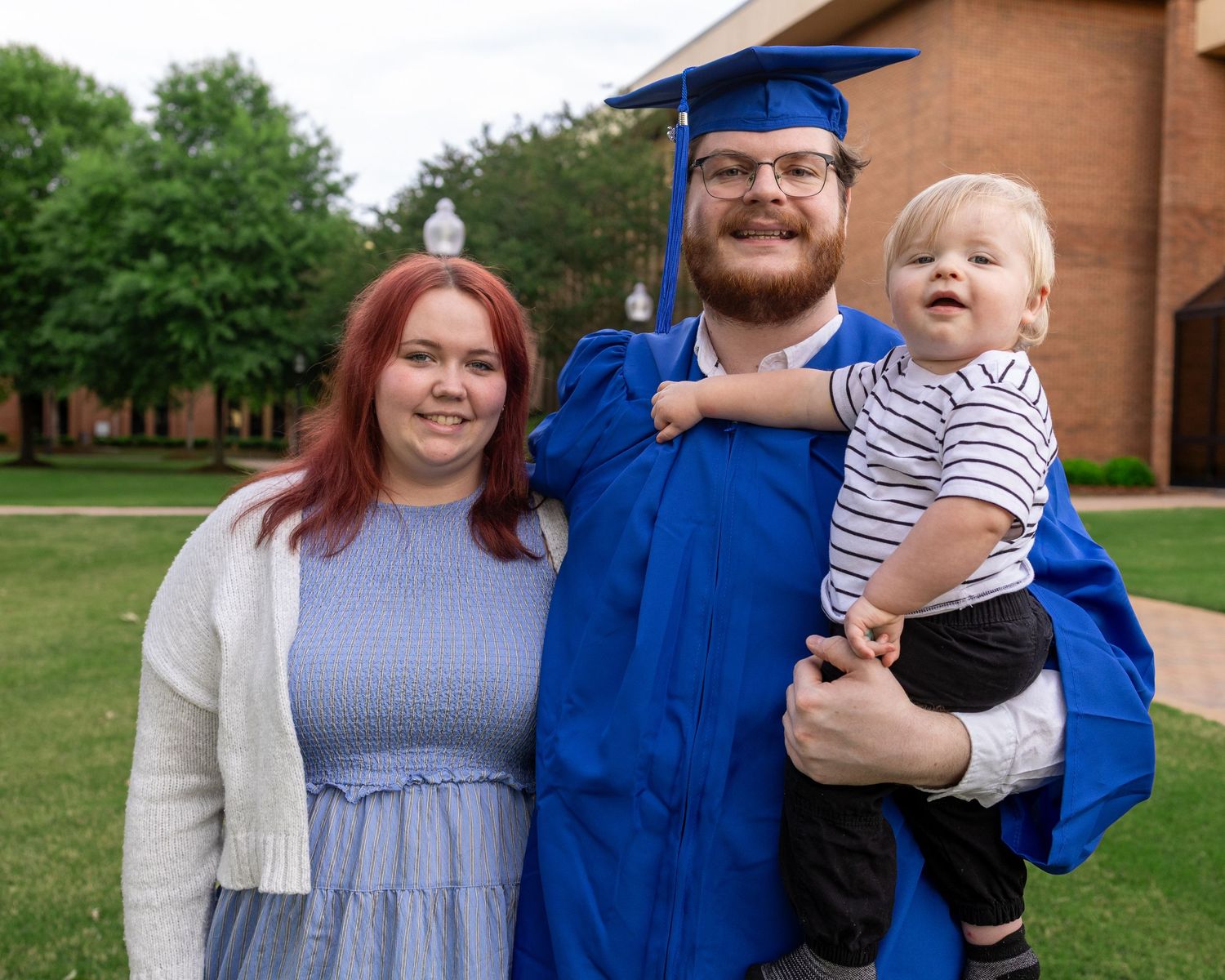 Graduate in a blue cap and gown posing with family during a senior photography session near Madison, Alabama.