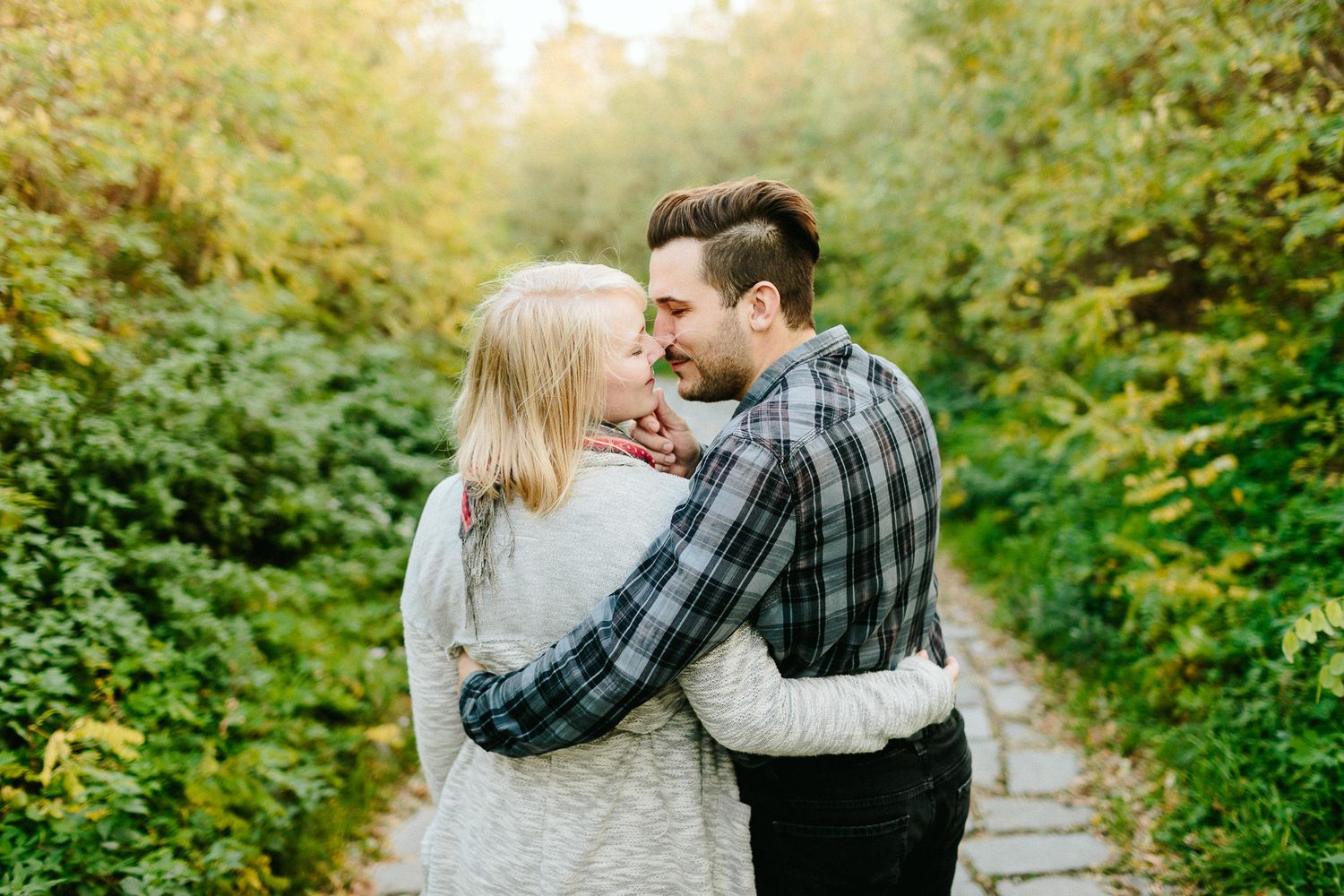 A couple sharing a romantic moment on a tree-lined path surrounded by lush greenery.