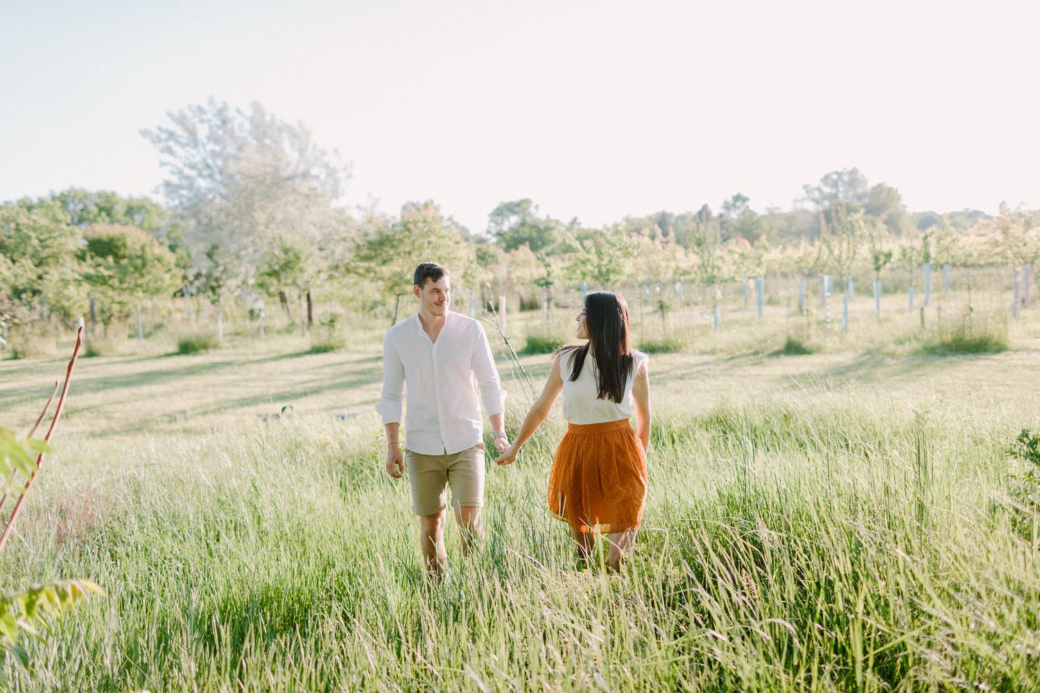 Couple holding hands while walking through a lush green meadow on a sunny day.