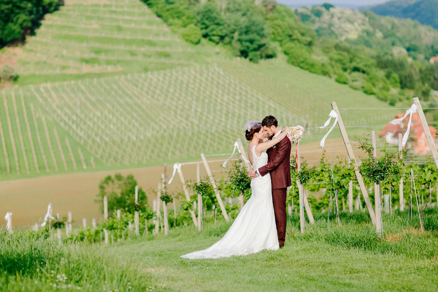 Bride and groom embrace romantically in a scenic vineyard with rolling green hills in background.