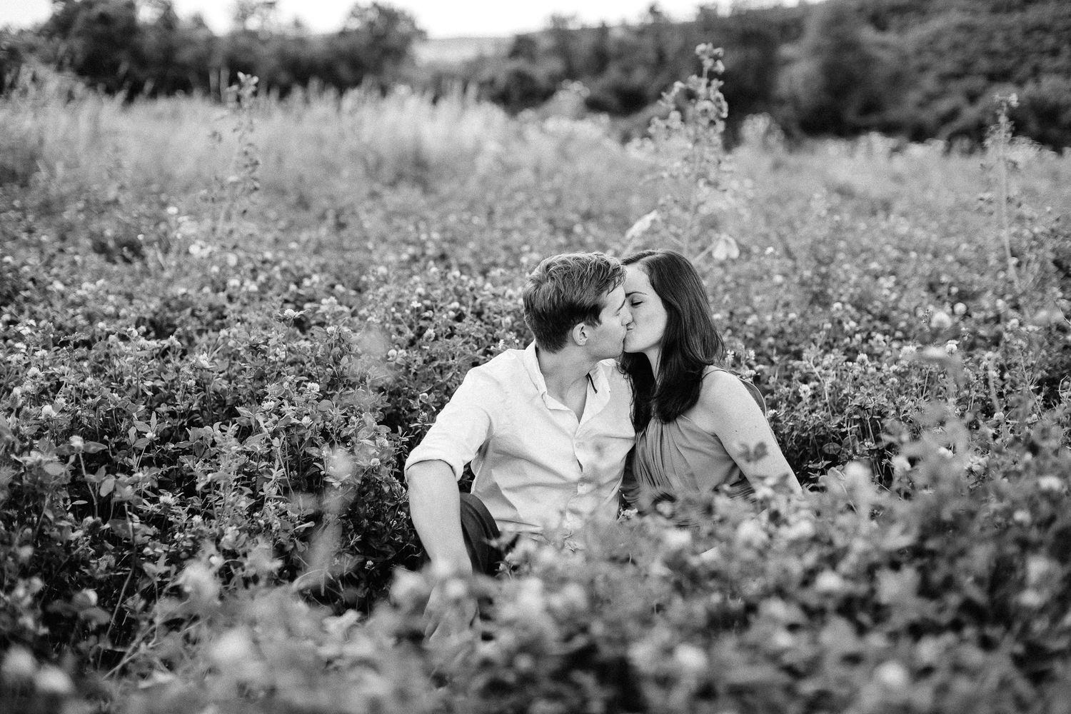 Black and white photo of couple kissing while sitting in a blooming flower field.