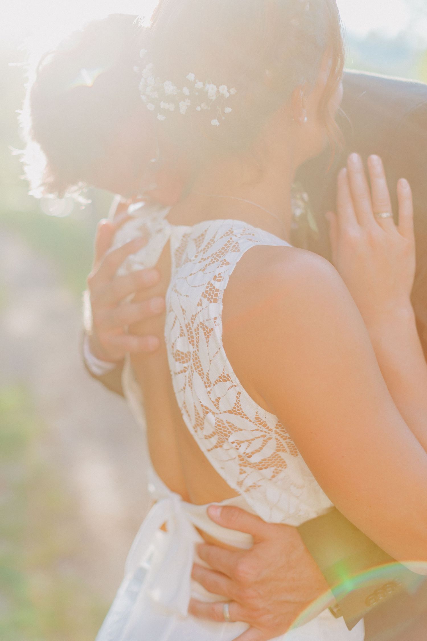Couple sharing tender embrace in warm sunlight, bride wearing elegant lace open-back gown.
