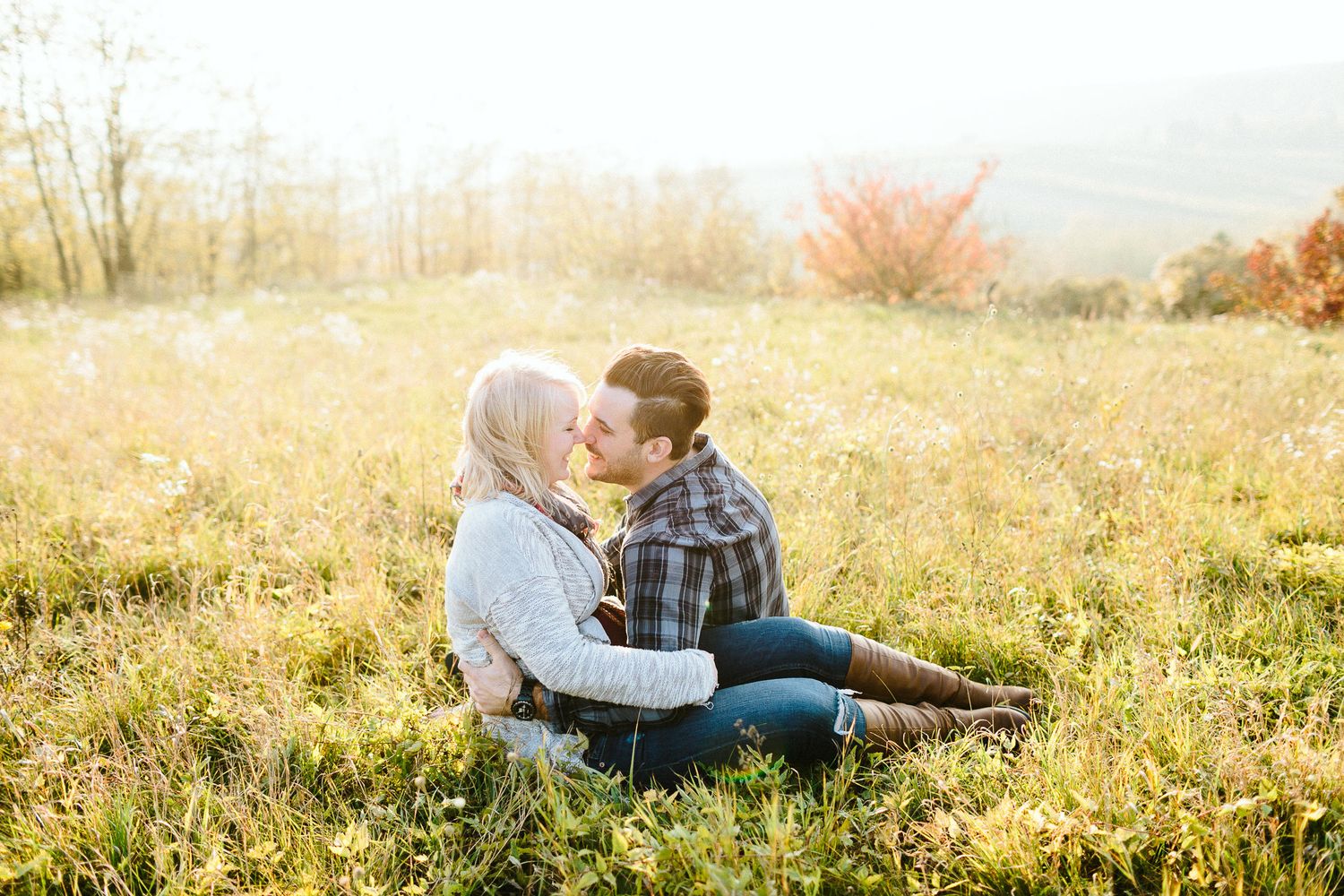 A couple sharing a kiss while sitting in a golden autumn field at sunset.