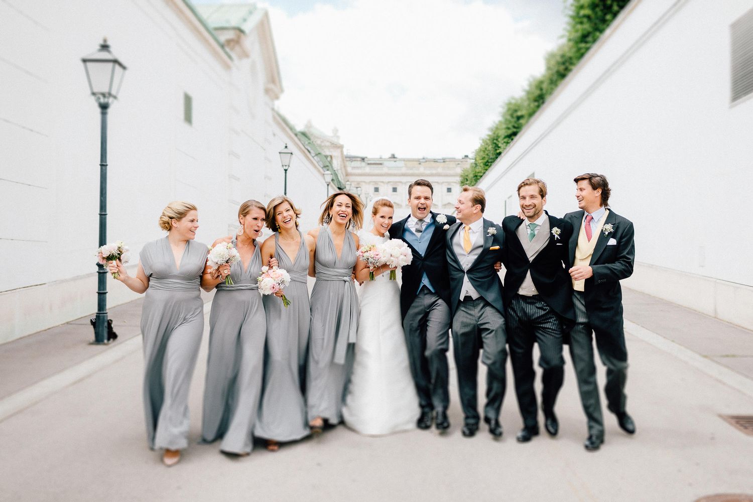 Wedding party walking together in gray bridesmaid dresses and dark suits along a cobblestone street.