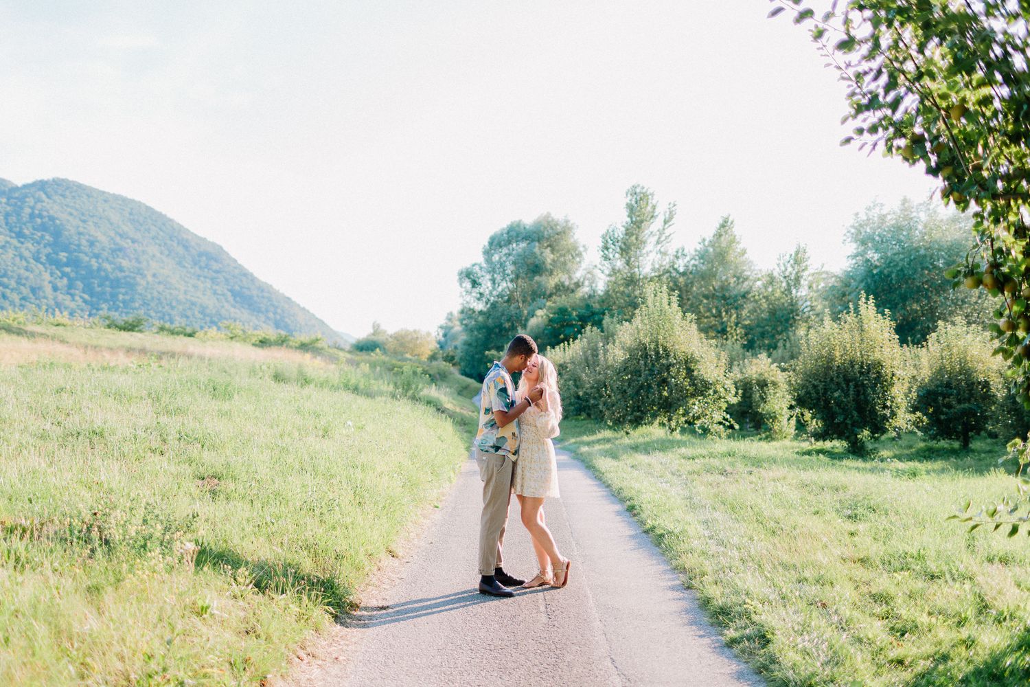 Couple sharing a romantic kiss on a quiet country road surrounded by green hills.