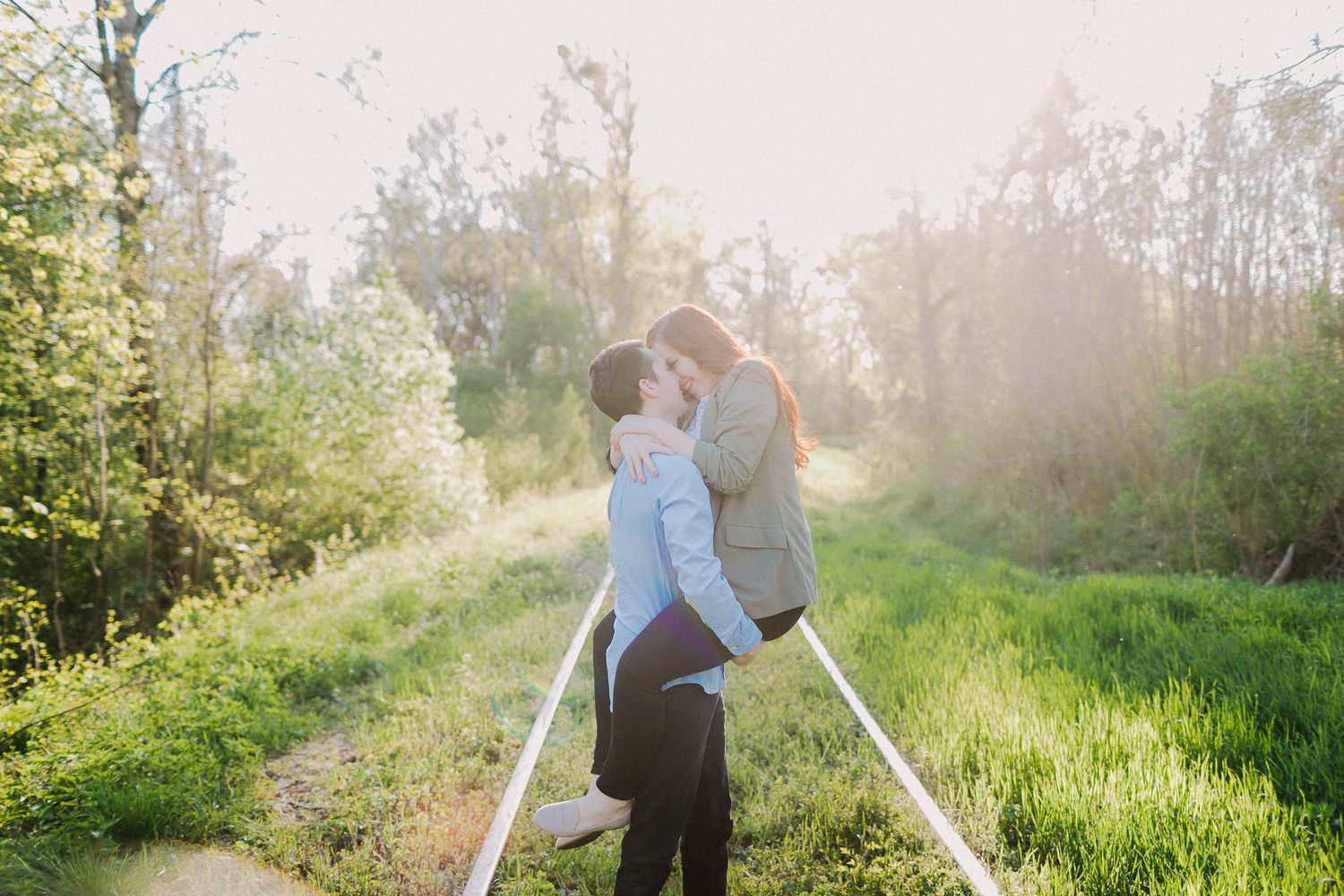 A couple sharing a joyful embrace on railway tracks surrounded by lush greenery.