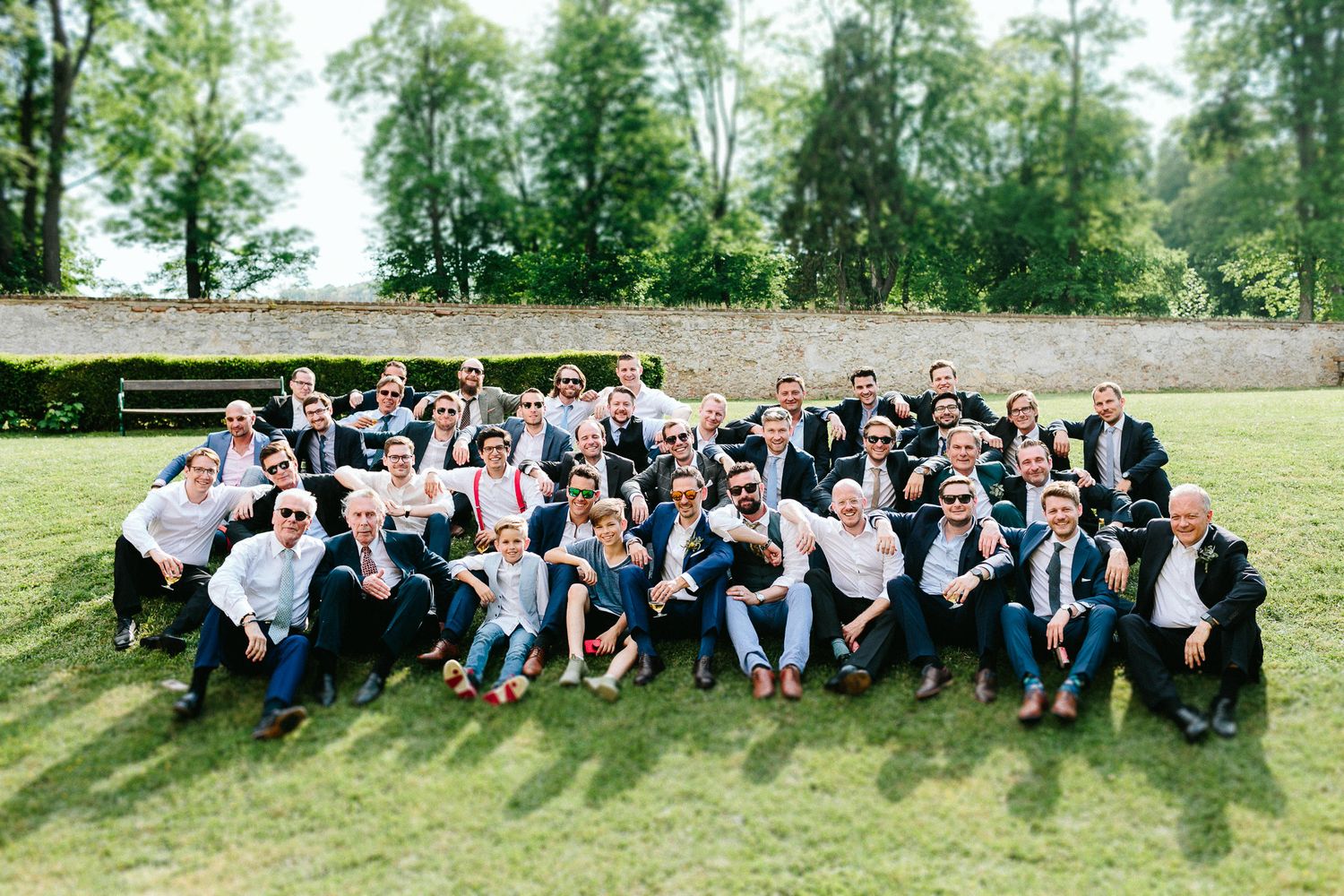 Large wedding party group photo on green lawn with guests posing and celebrating outdoors.