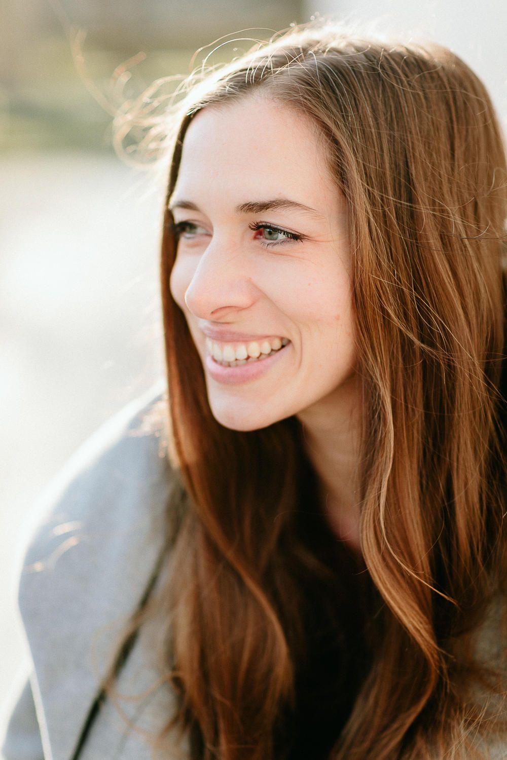 Smiling young woman with long auburn hair and blue eyes in natural outdoor light.