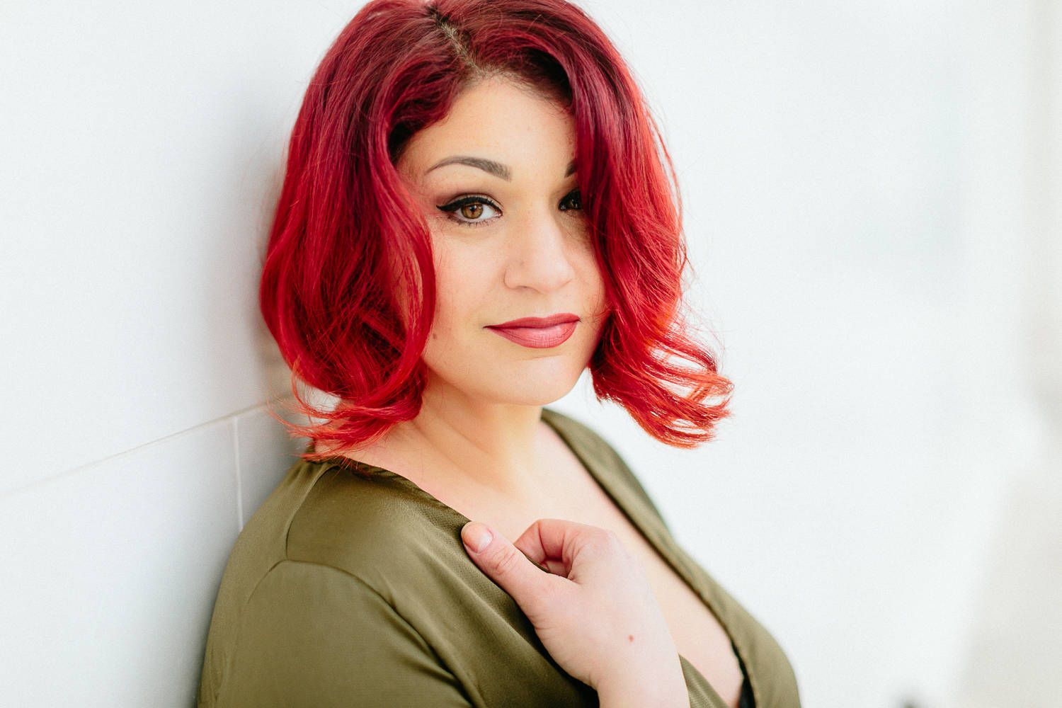 Woman with vibrant red hair and red lips posing in an olive green top.