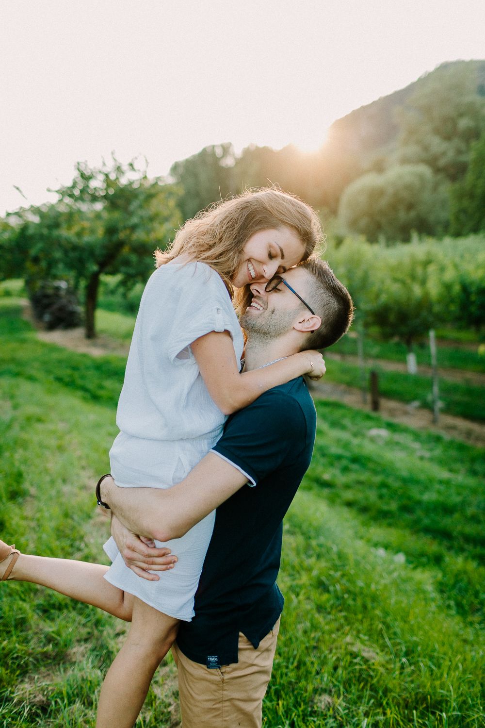 Joyful couple embracing at sunset in a lush green vineyard landscape.