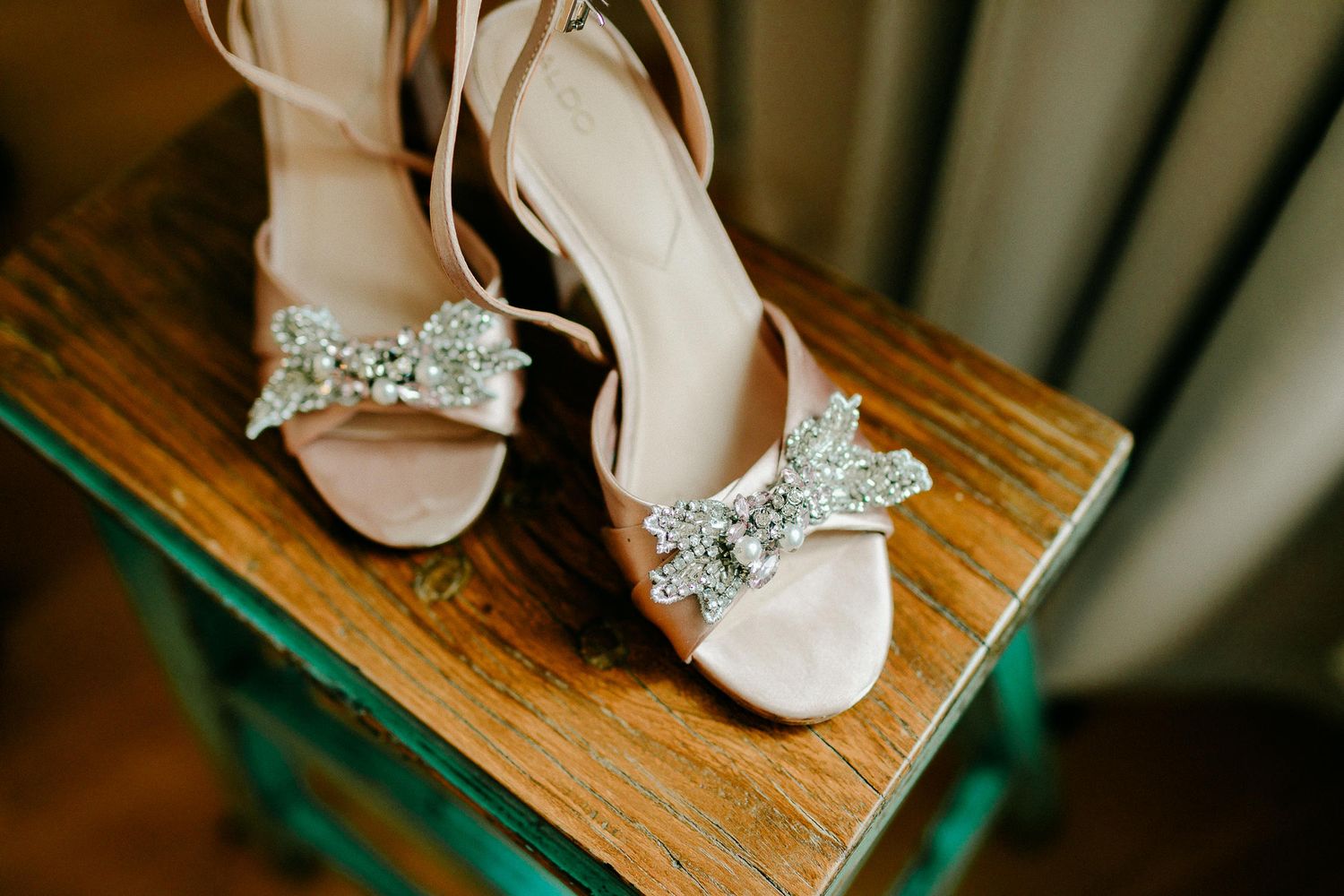 Elegant bridal heels with silver glitter bow detail displayed on rustic wooden stool.