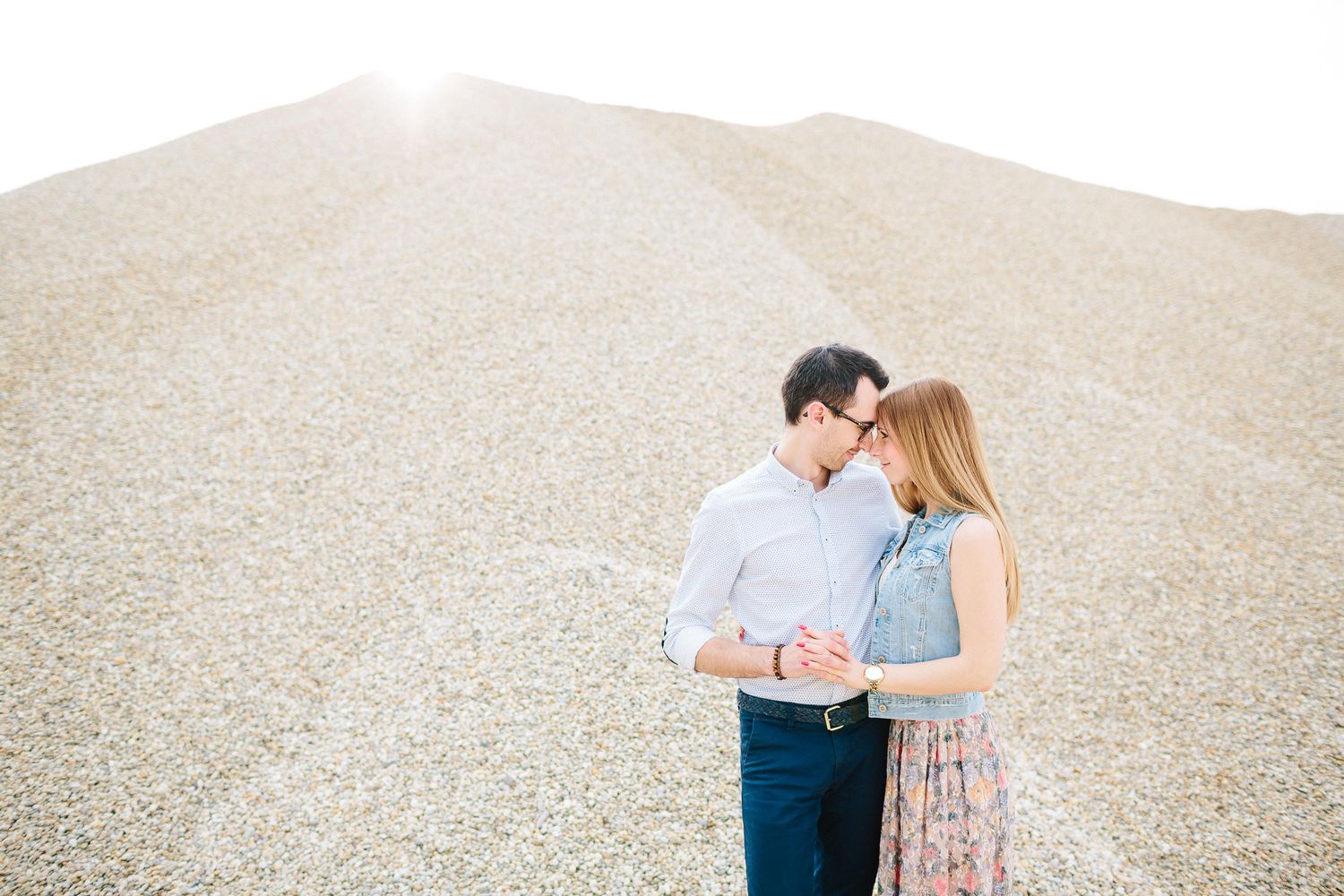 Couple embracing tenderly in front of a large gravel hill in bright sunlight.