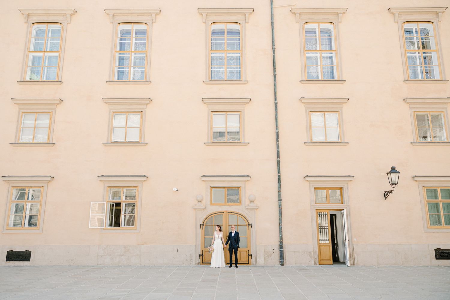 Wedding couple standing before a grand pink European building facade on their special day.