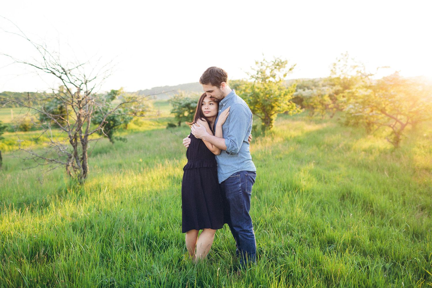 Man tenderly embracing woman in black dress in a sunlit green meadow.