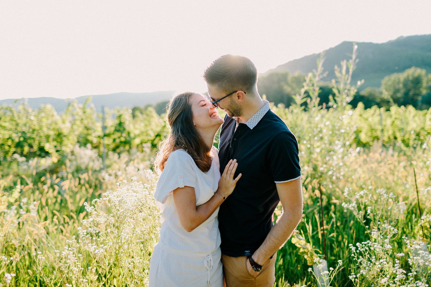 A couple sharing a romantic moment in a sunlit wildflower field with mountain views.