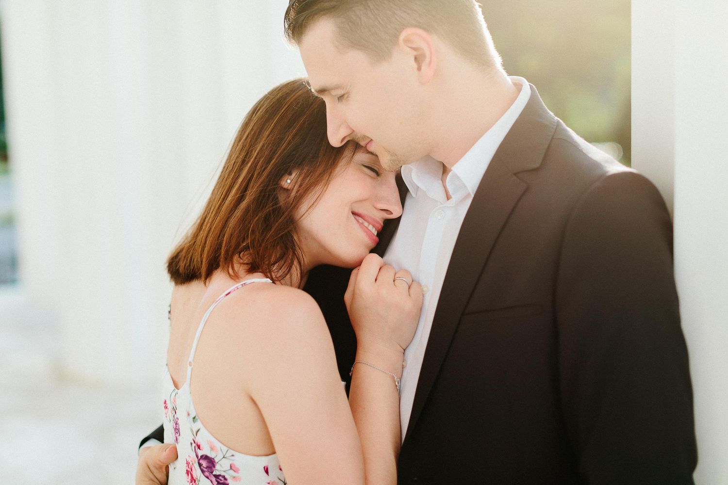 Couple sharing an intimate moment leaning close together outdoors near white classical columns.