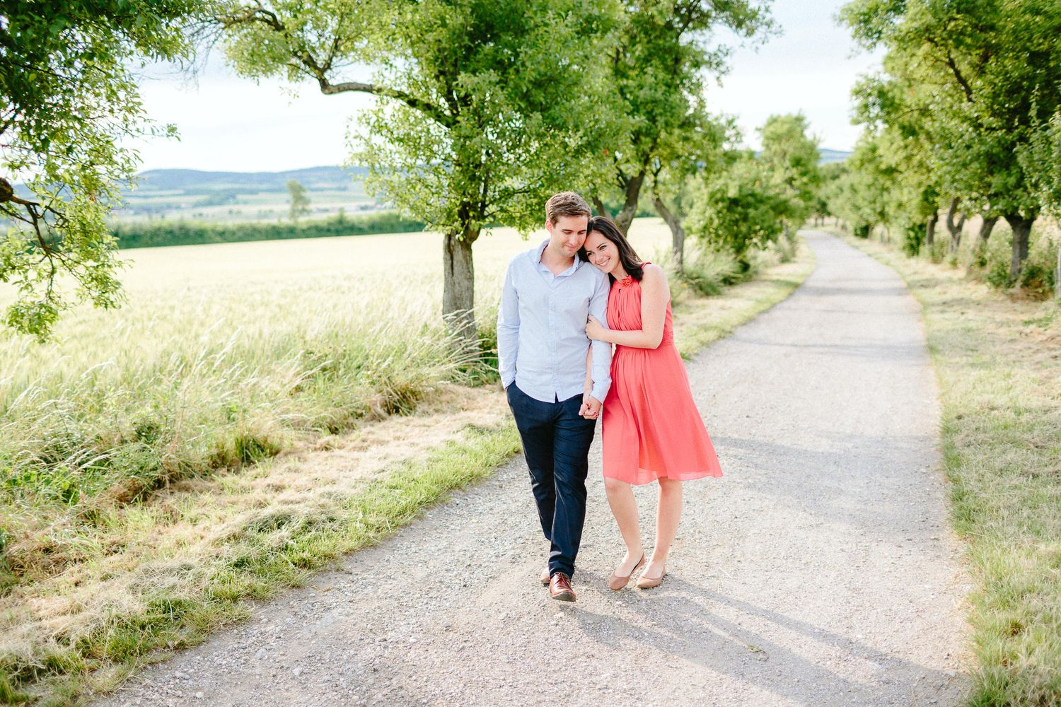 Romantic couple walking hand in hand down a scenic tree-lined country path.
