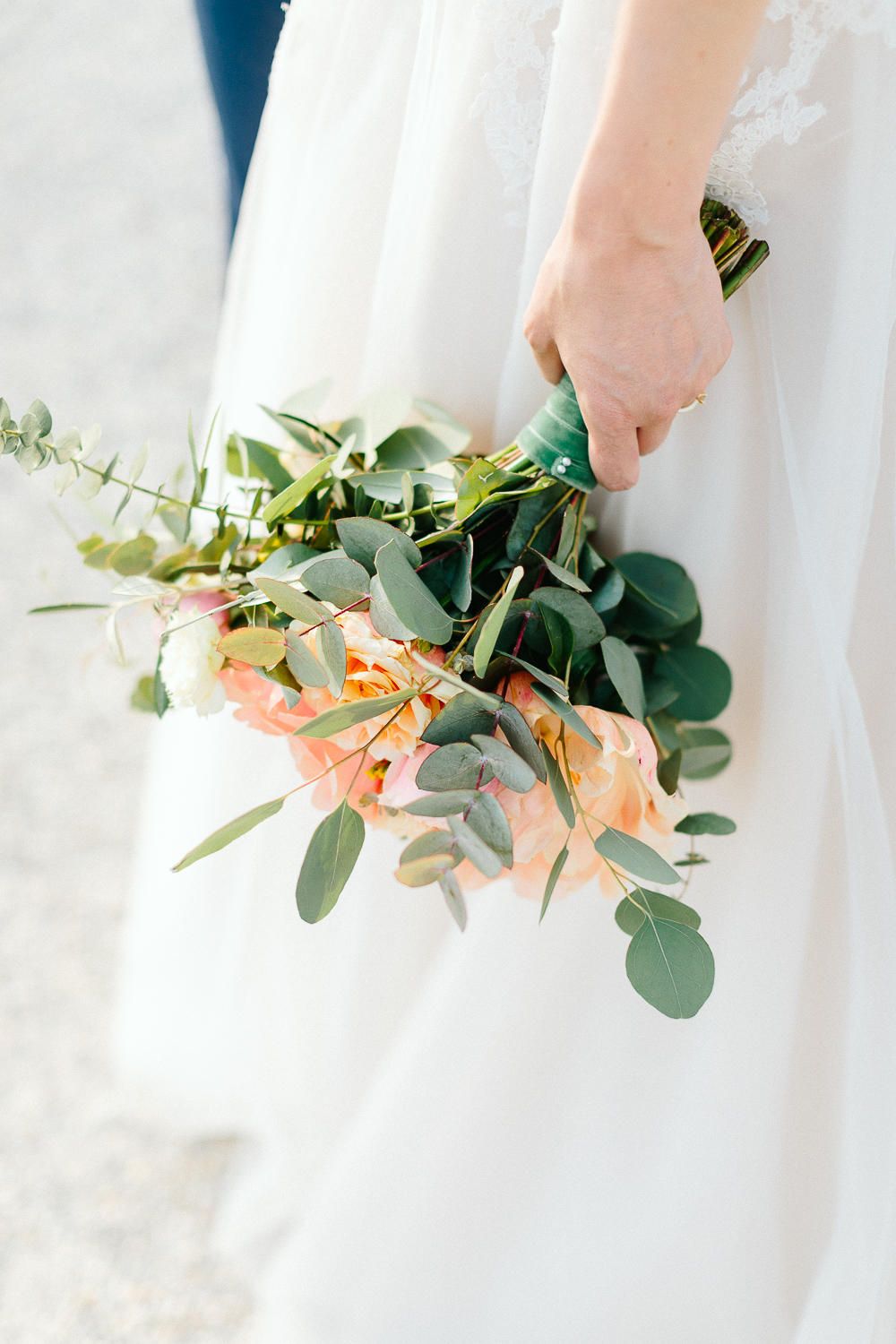 Close-up of a bride holding a wedding bouquet with peach roses and eucalyptus greenery.