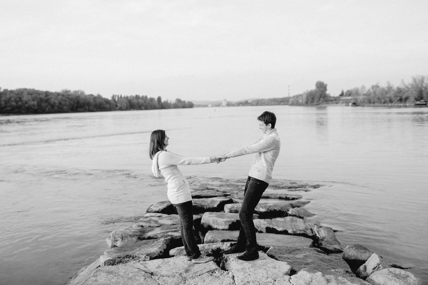 A couple holding hands on rocky riverbank in a black and white outdoor portrait.