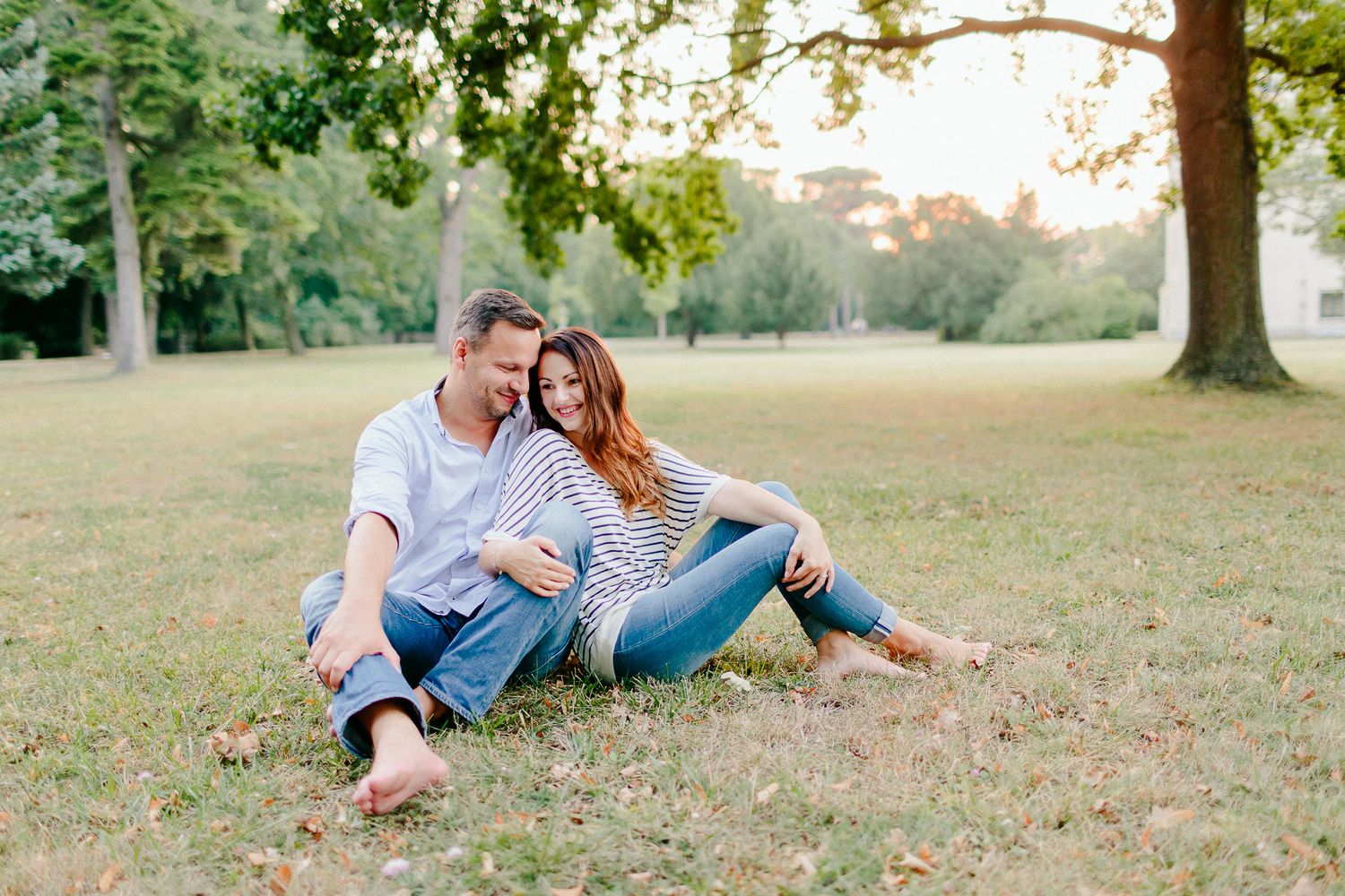 Couple sitting together on green grass in a sunny park, sharing a quiet moment.