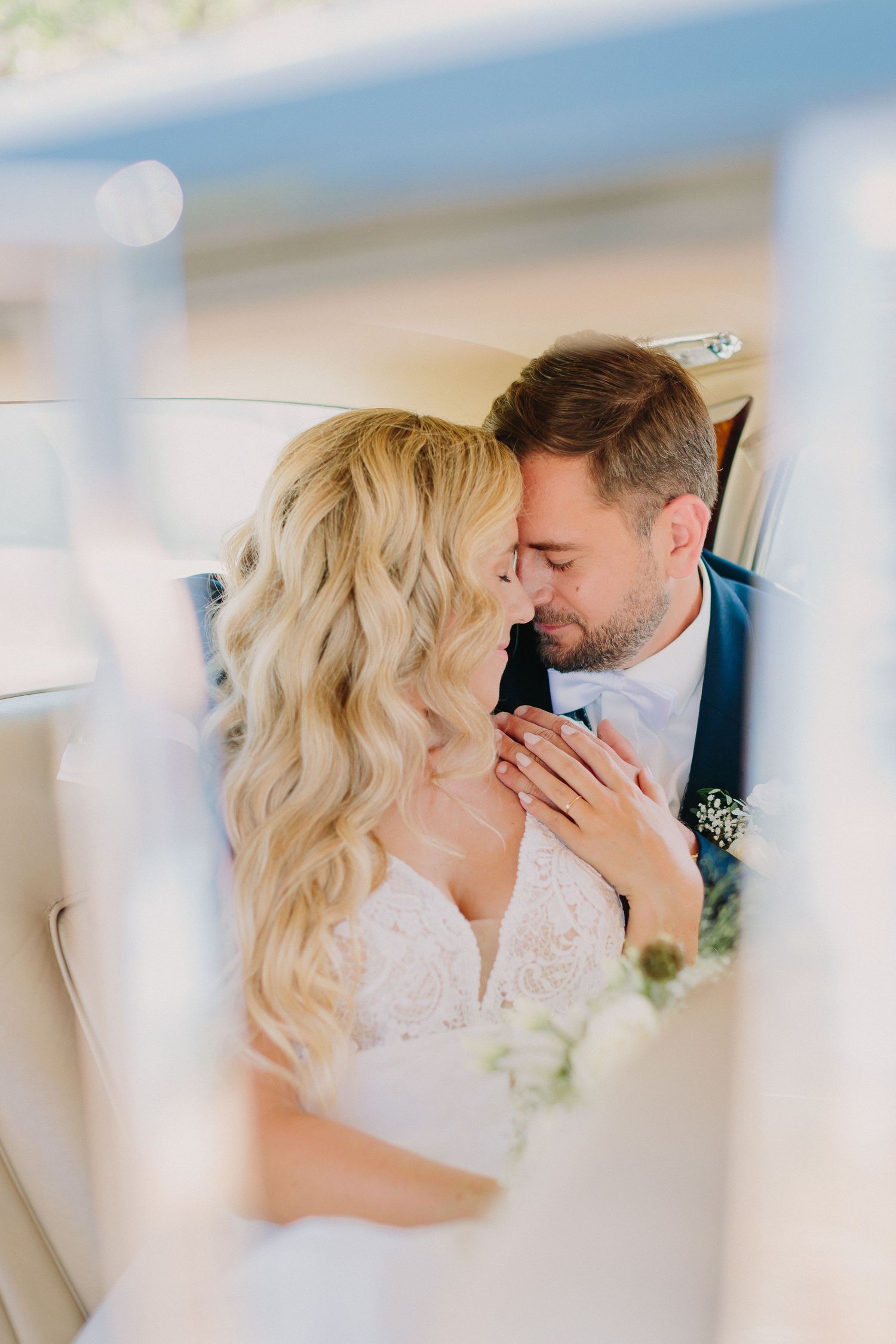 Bride and groom sharing a tender moment inside a vintage car, bride with flowing blonde curls.