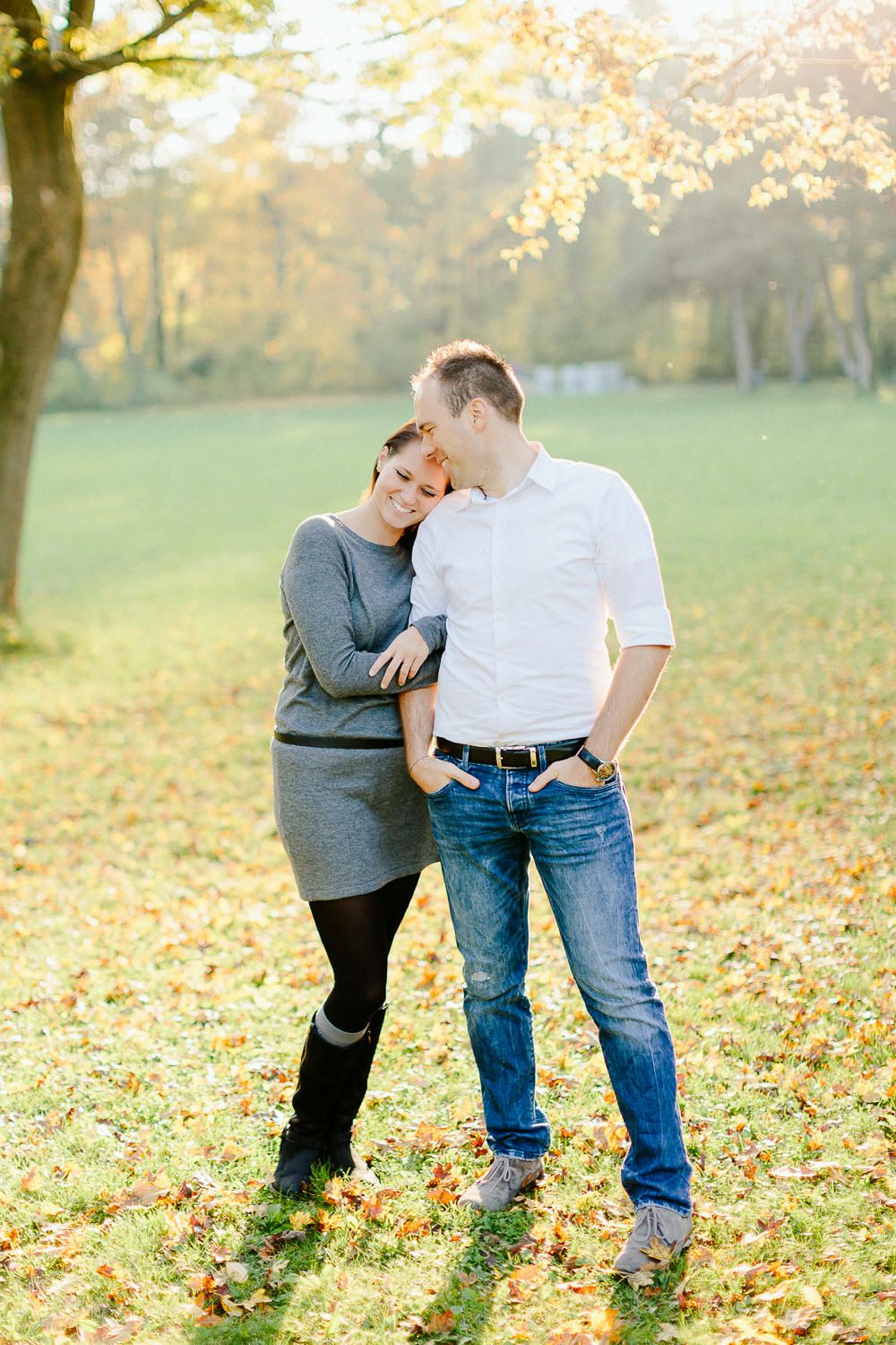 Couple cuddling in an autumn park with golden leaves scattered on the ground.