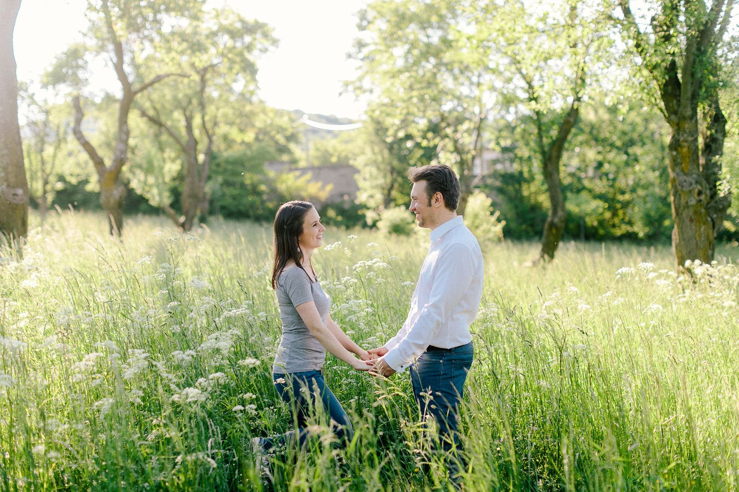Couple holding hands and facing each other in a sunlit wildflower meadow.