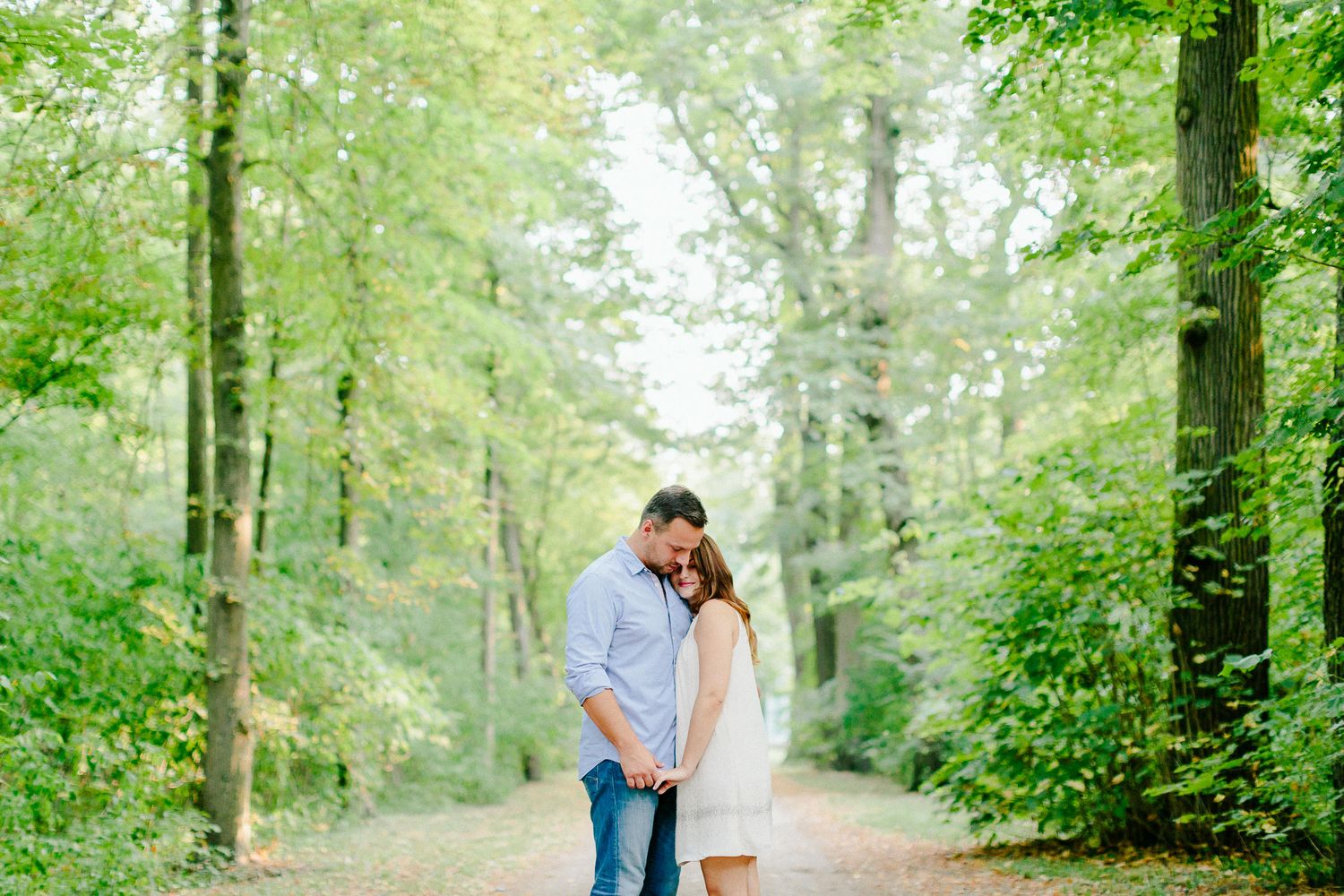 Couple embracing on a peaceful forest path surrounded by lush green trees.
