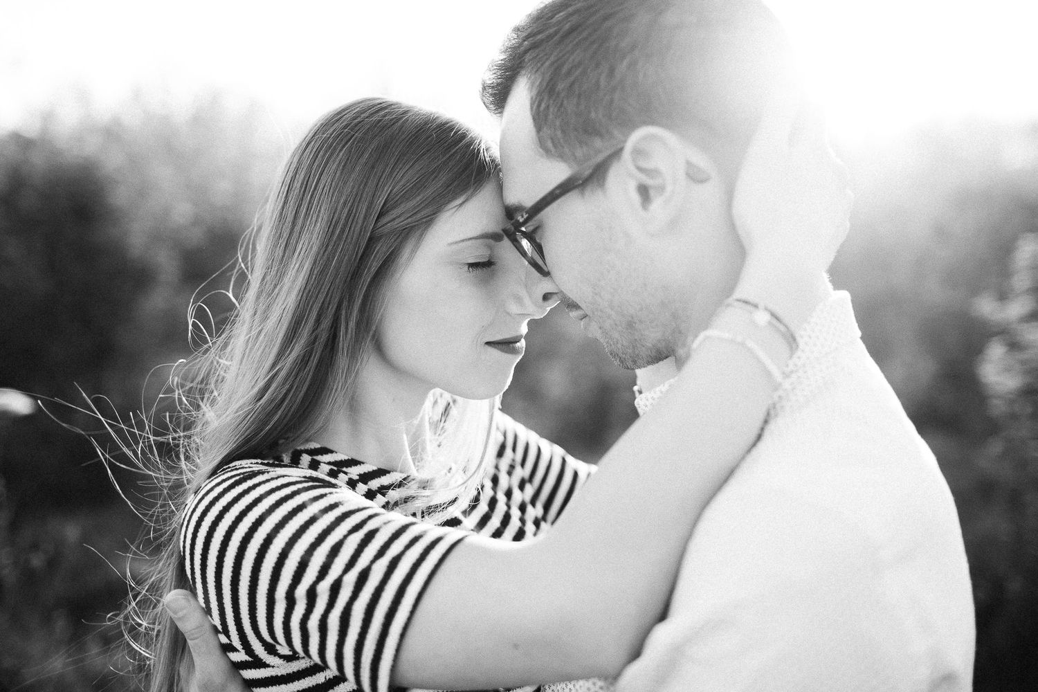 Black and white close-up of couple sharing an intimate moment in soft sunlight.