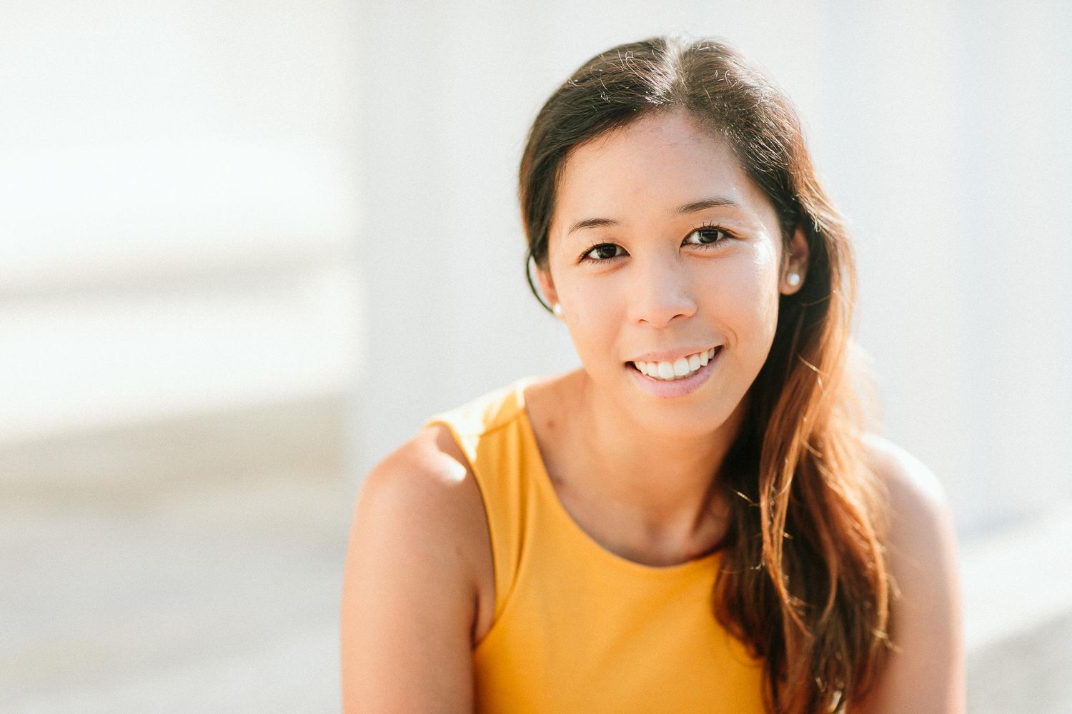 Smiling Asian woman in yellow tank top posing outdoors in bright natural light.