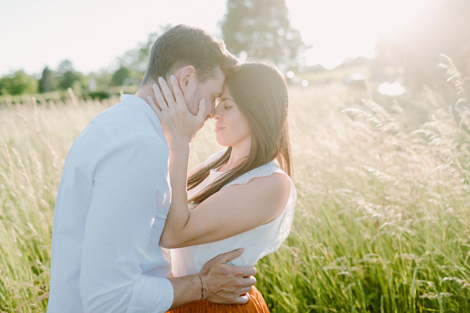 Couple sharing an intimate moment in a sunlit field of tall golden grass.
